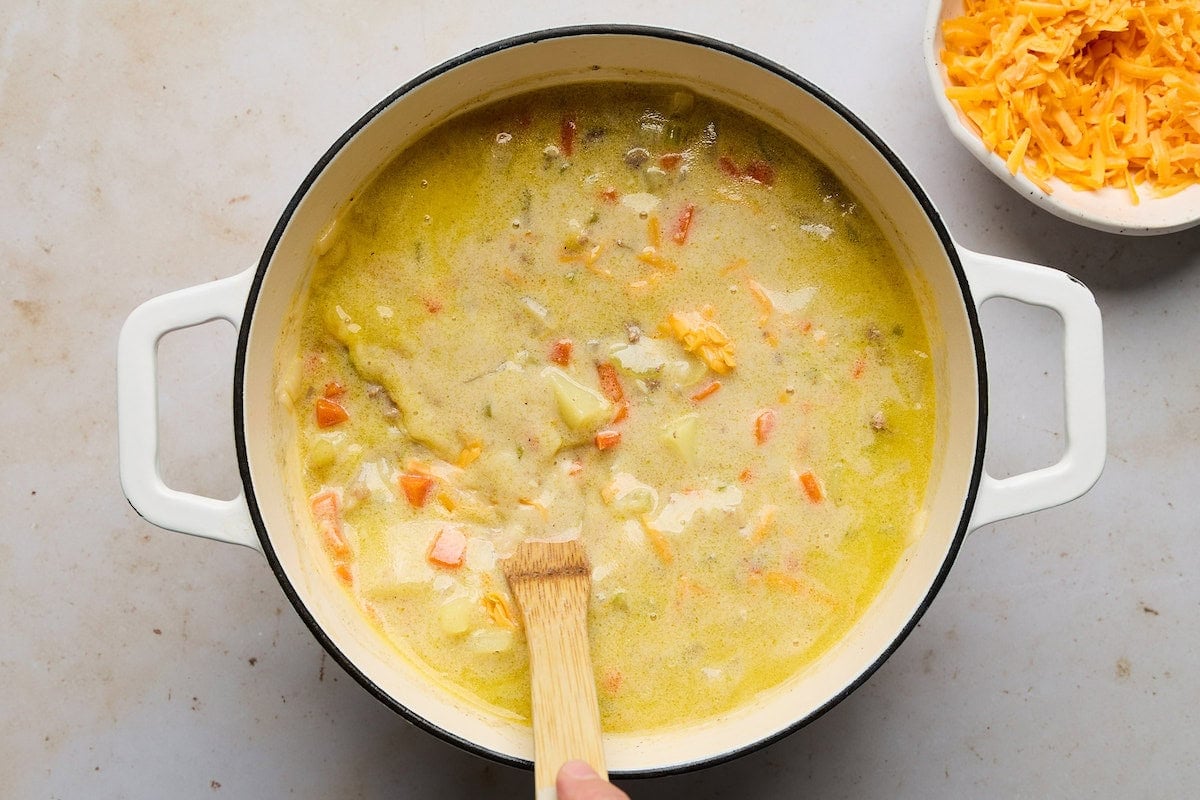 cheeseburger soup in pot being stirred with wooden spoon.