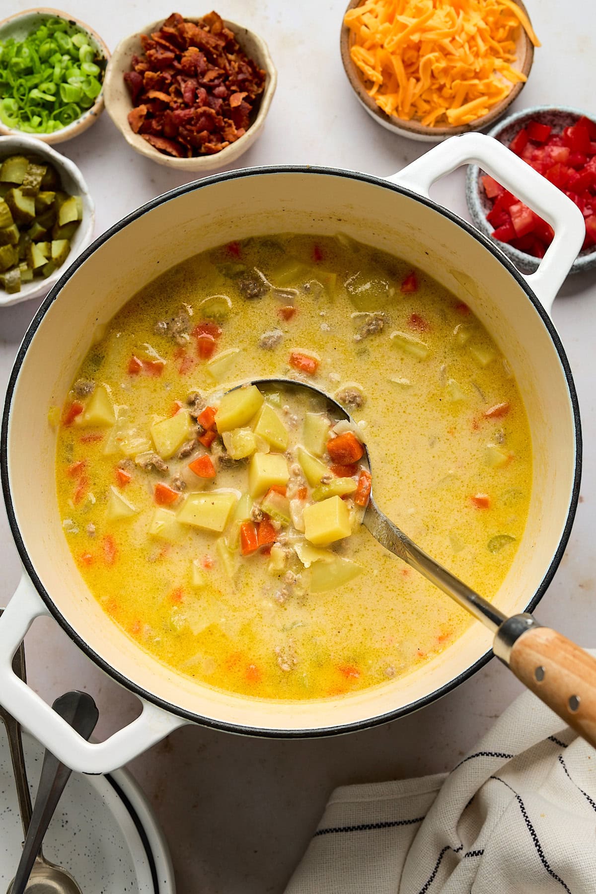 cheeseburger soup in pot with serving spoon with toppings in small bowls.