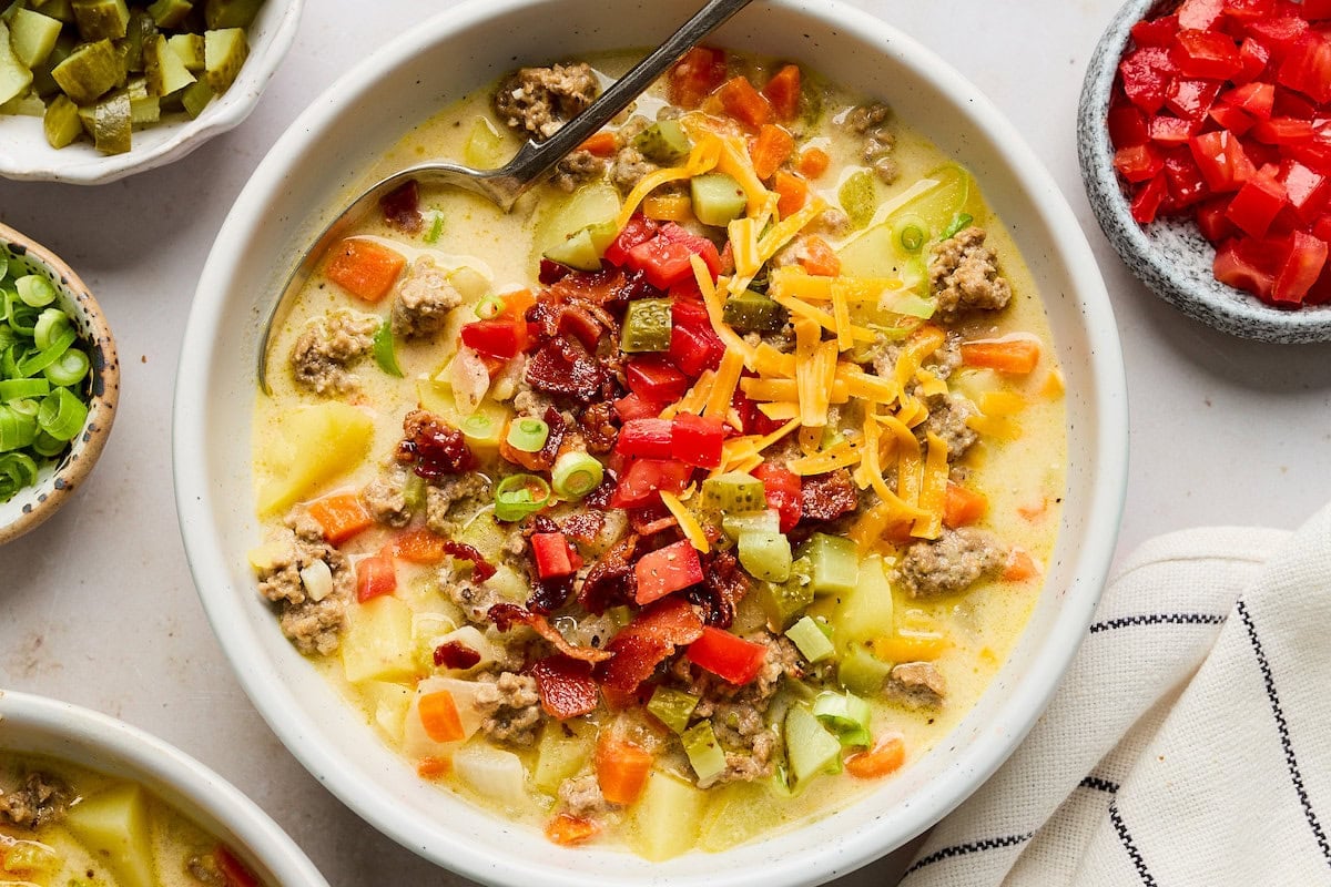 cheeseburger soup in bowl with toppings and spoon.