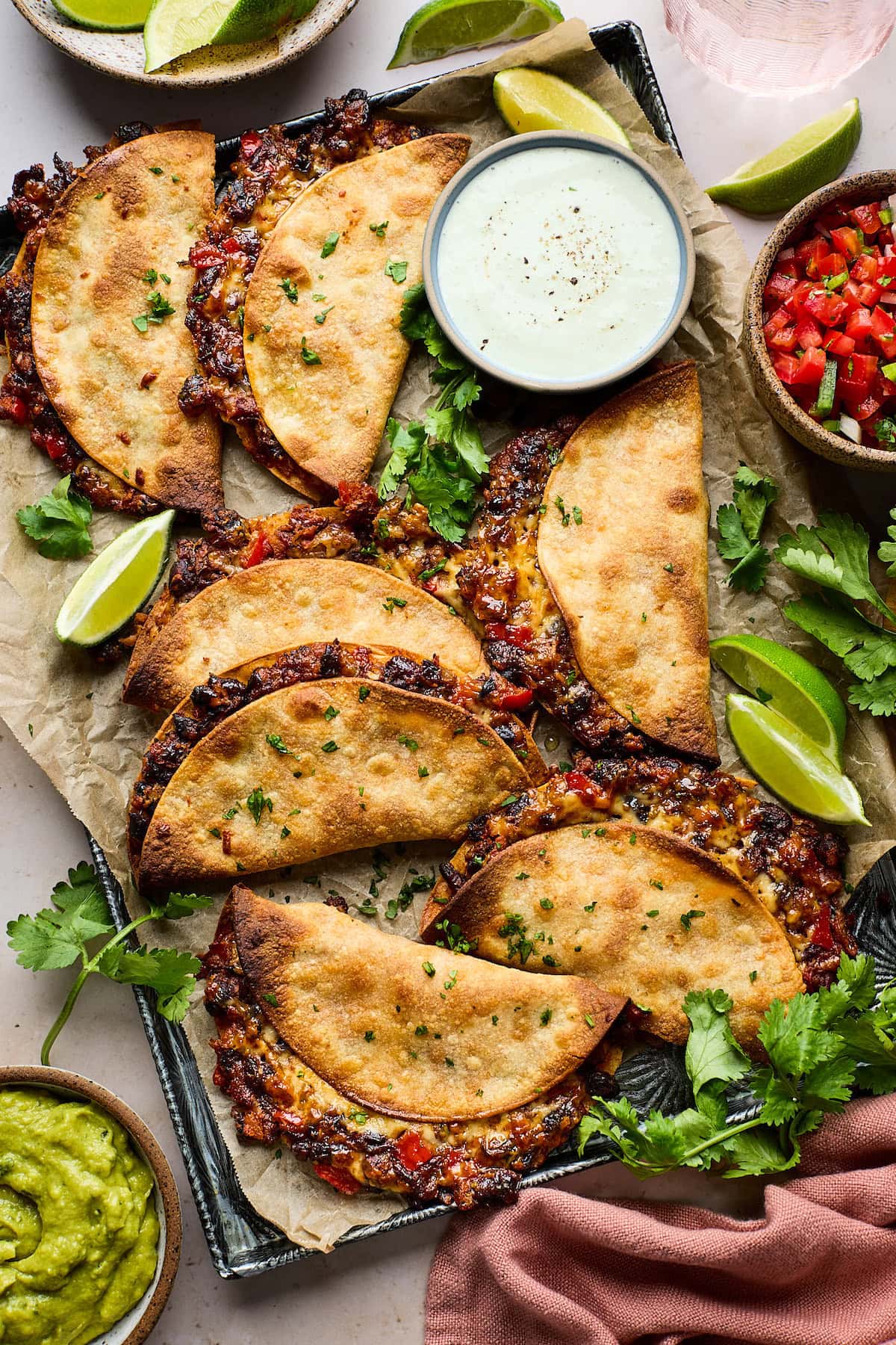 crispy black bean tacos on sheet pan with jalapeño ranch, lime wedges, cilantro, and pico de gallo.