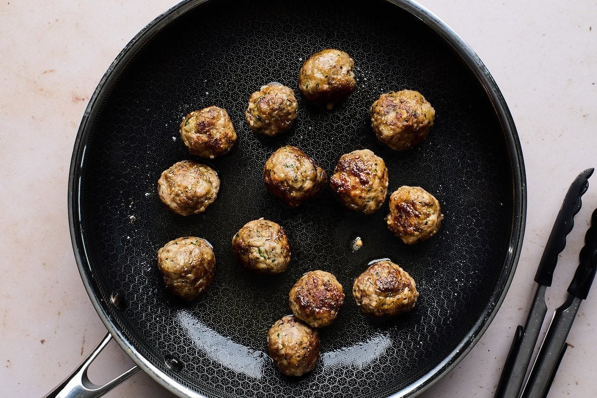 meatballs cooking in skillet for meatball orzo soup.
