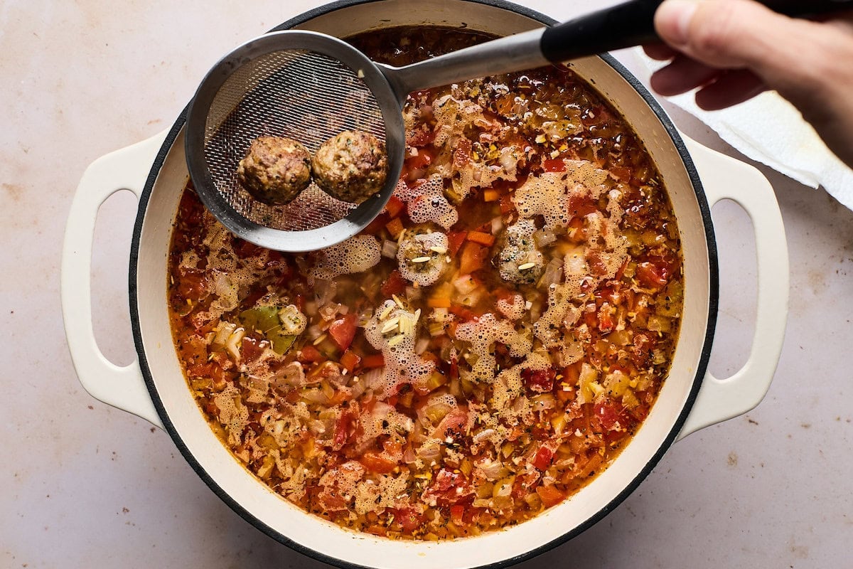 meatballs being added into pot of meatball orzo soup.