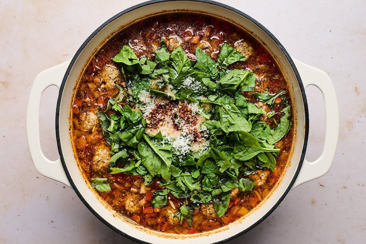 meatball orzo soup in pot with spinach and parmesan cheese.