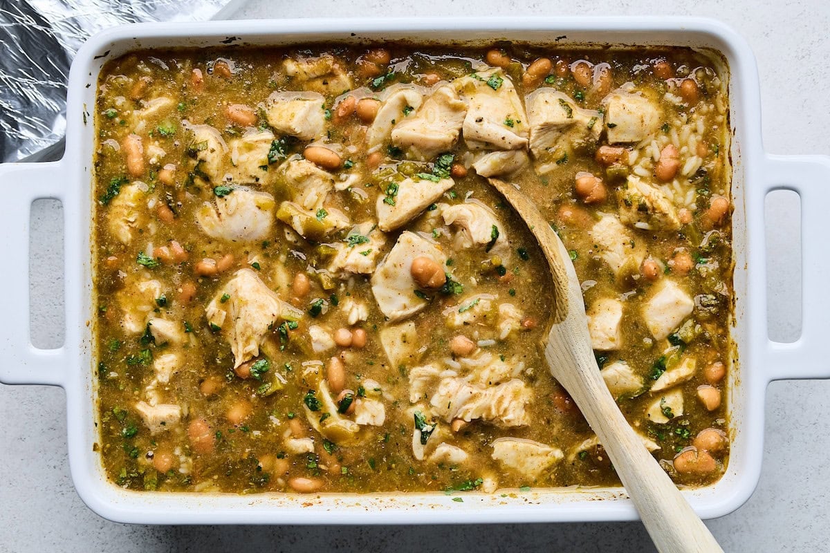 salsa verde chicken and rice ingredients being stirred in pan with wooden spoon.
