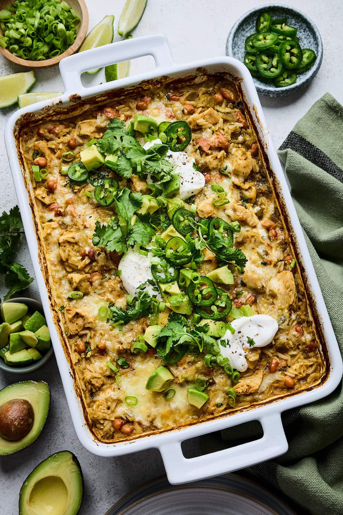 salsa verde chicken and rice in baking dish with cilantro, avocado, jalapeño slices, and sour cream.