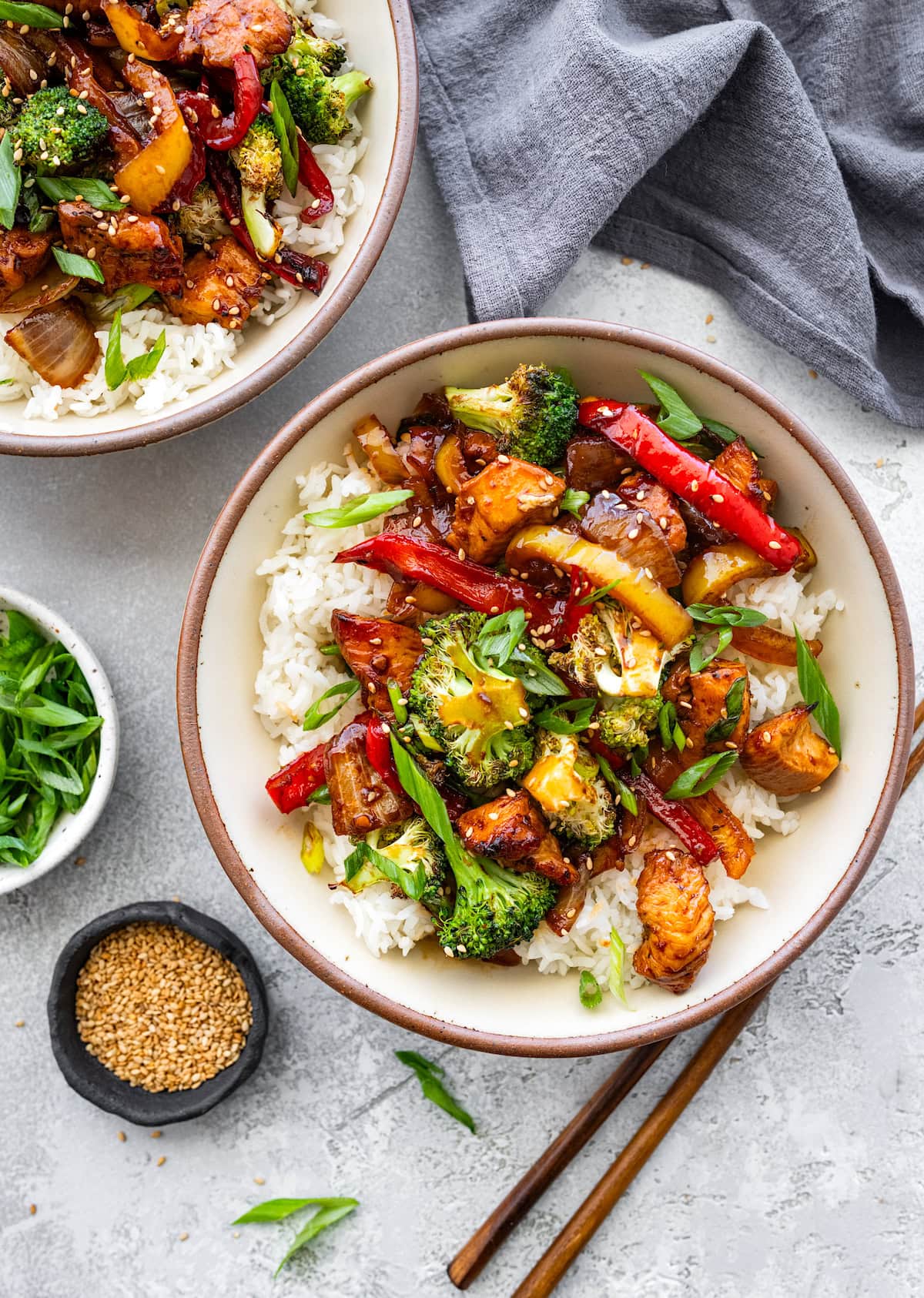 sheet pan chicken stir fry with rice in bowls topped with green onion and sesame seeds.