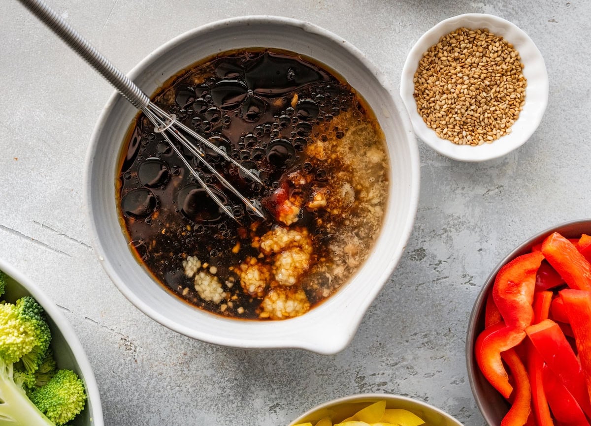 honey garlic sauce in bowl with whisk for sheet pan chicken stir fry.