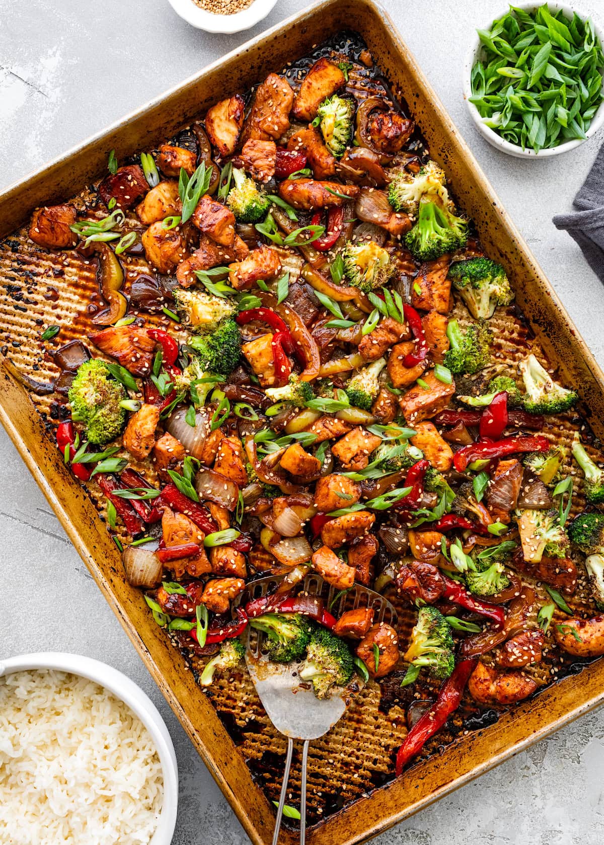 sheet pan chicken stir fry with broccoli, peppers, onion, honey garlic sauce, green onions, and sesame seeds.