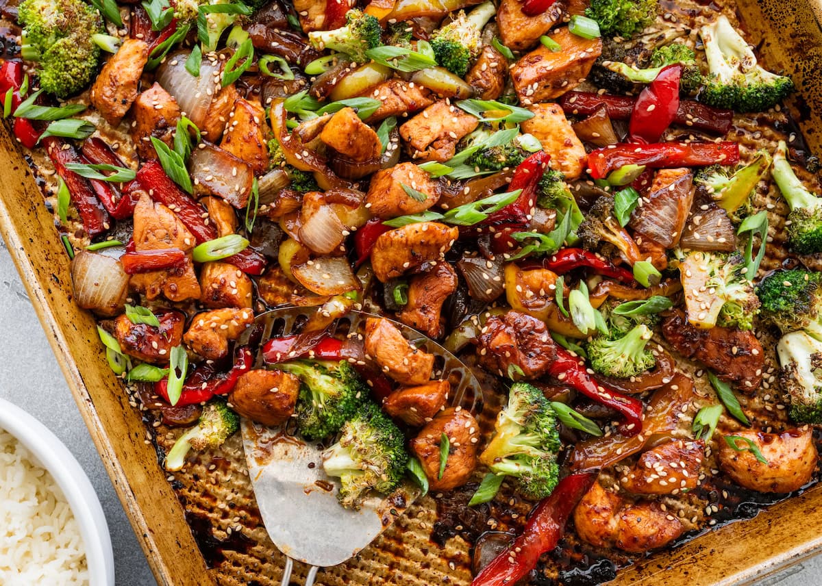 sheet pan chicken stir fry with veggies on sheet pan with spatula.