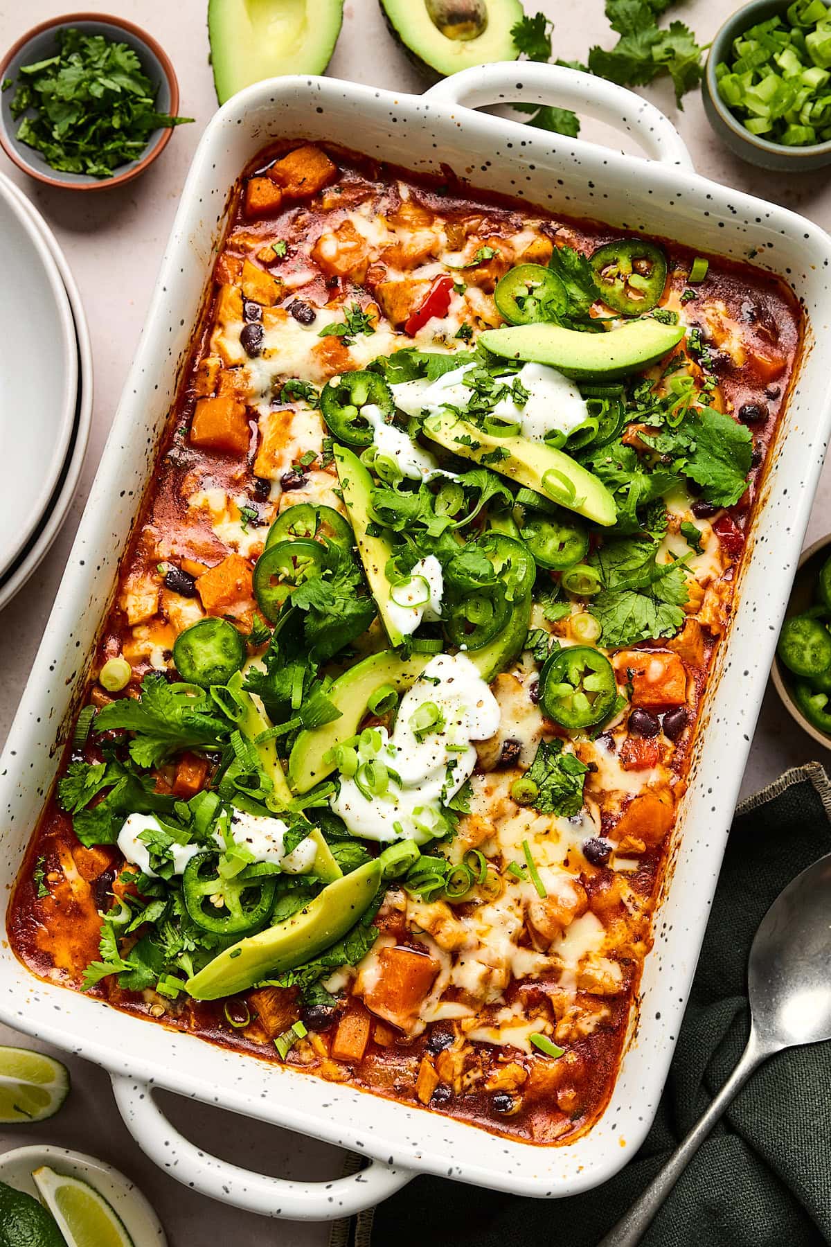 sweet potato chicken enchilada bake in baking dish topped with cilantro, avocado slices, jalapeño slices, green onion, and sour cream.