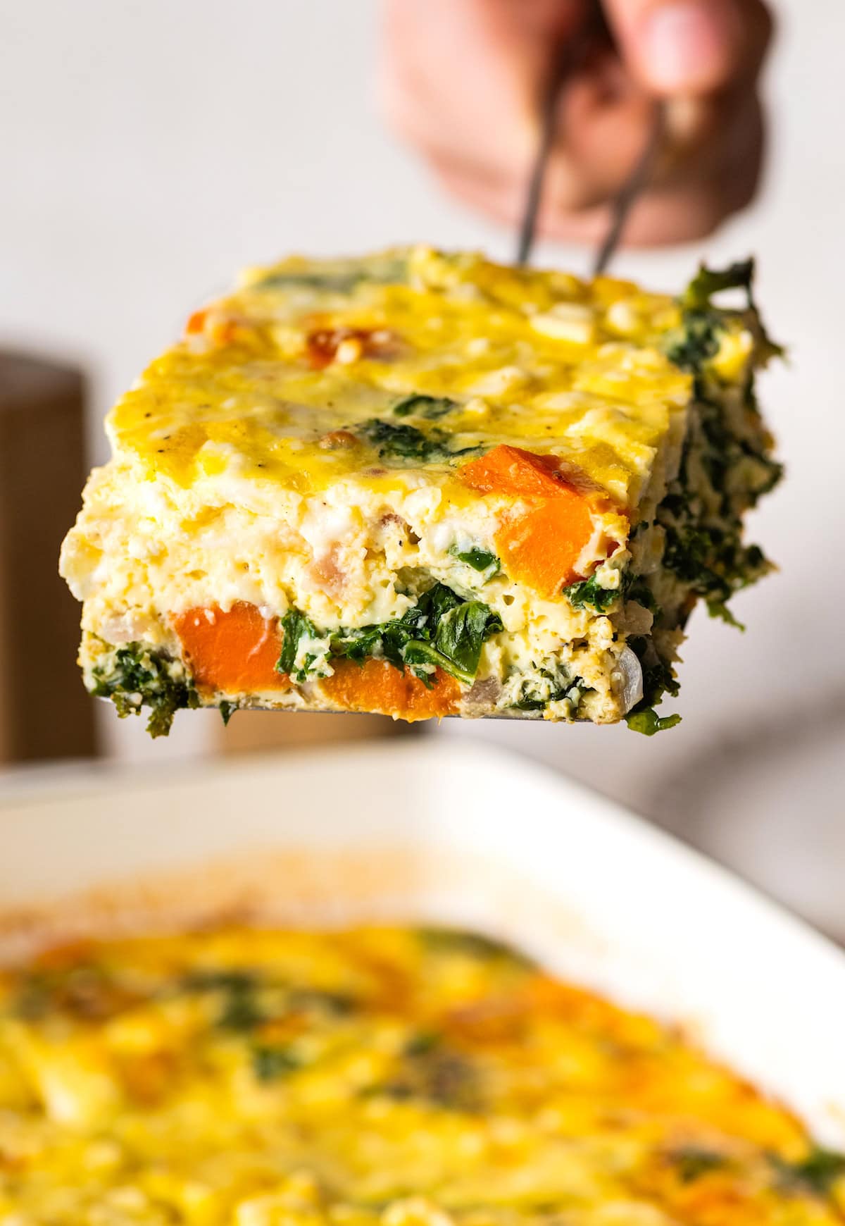 piece of sweet potato kale breakfast casserole being lifted out of the pan with a spatula.