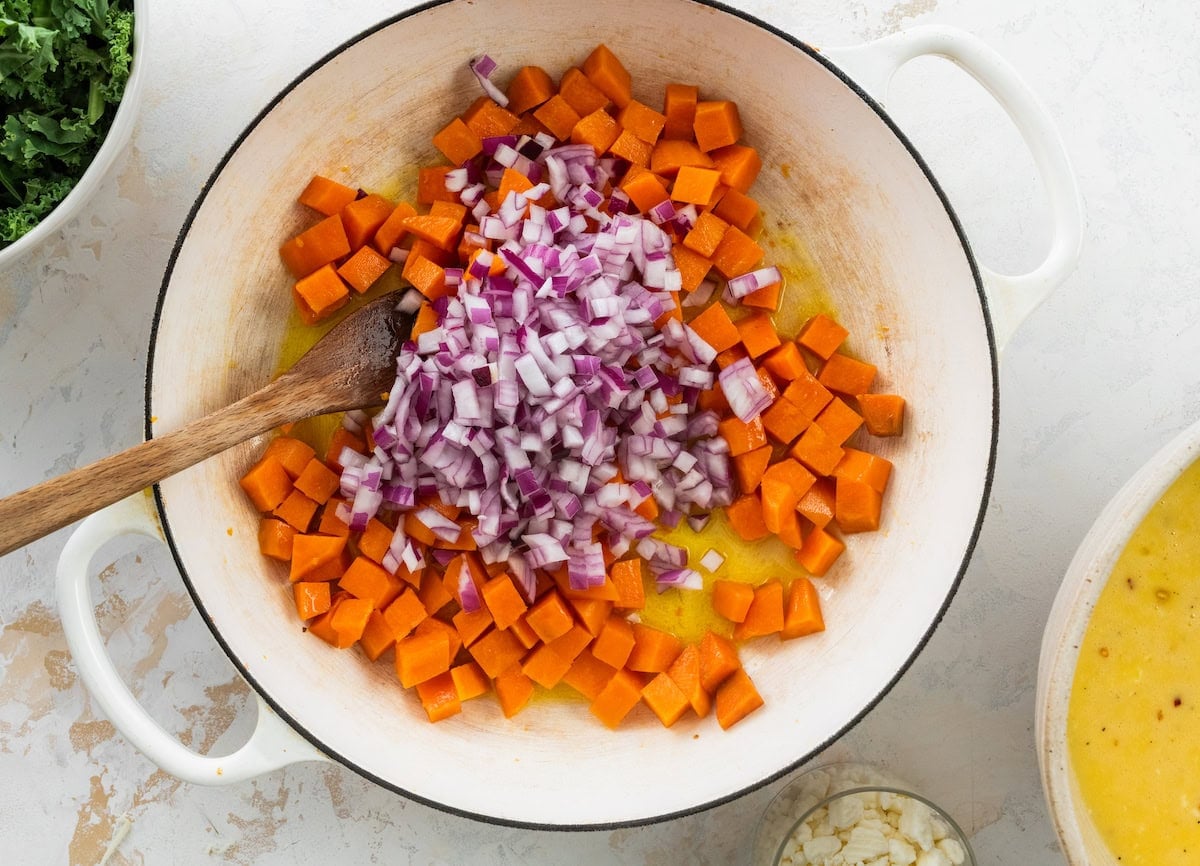 sweet potatoes and red onion cooking in skillet with wooden spoon.
