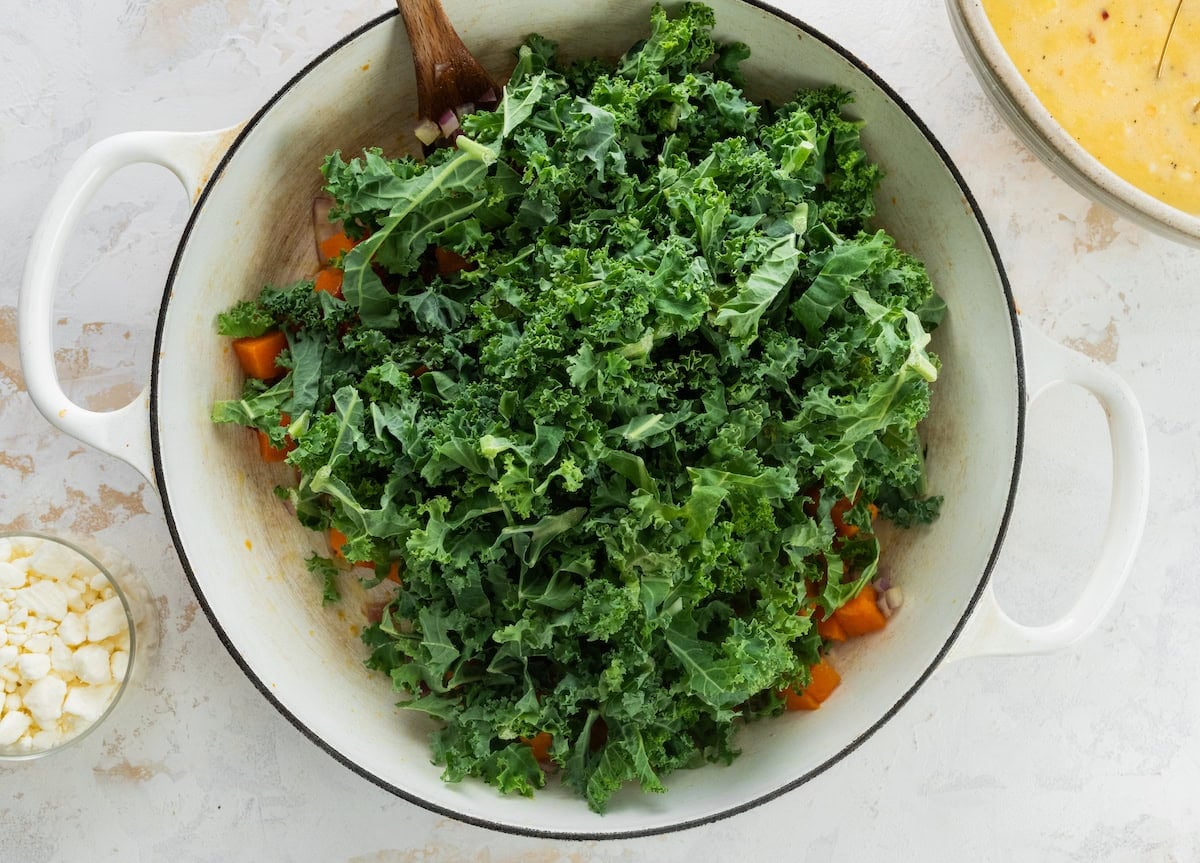 kale being added to skillet with sweet potatoes and red onion to make sweet potato kale breakfast casserole.