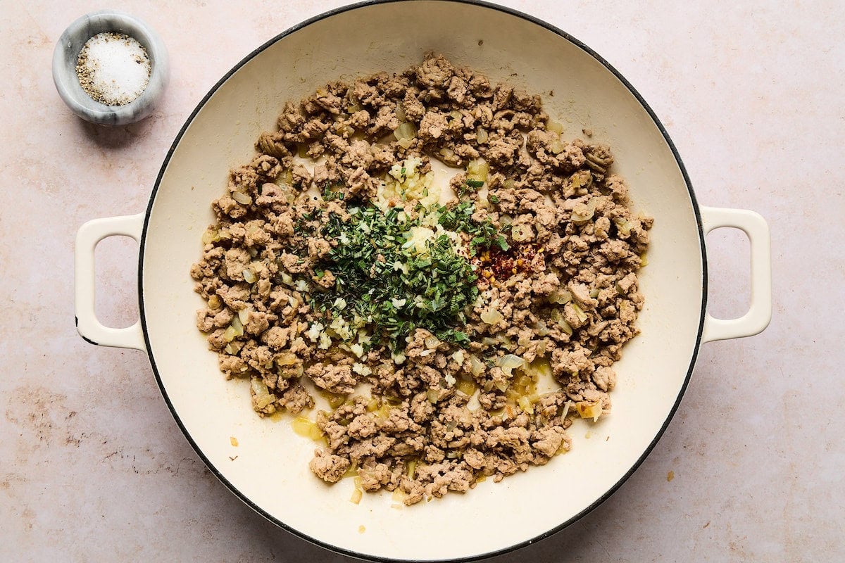 ground turkey cooking in skillet with fresh herbs and spices.