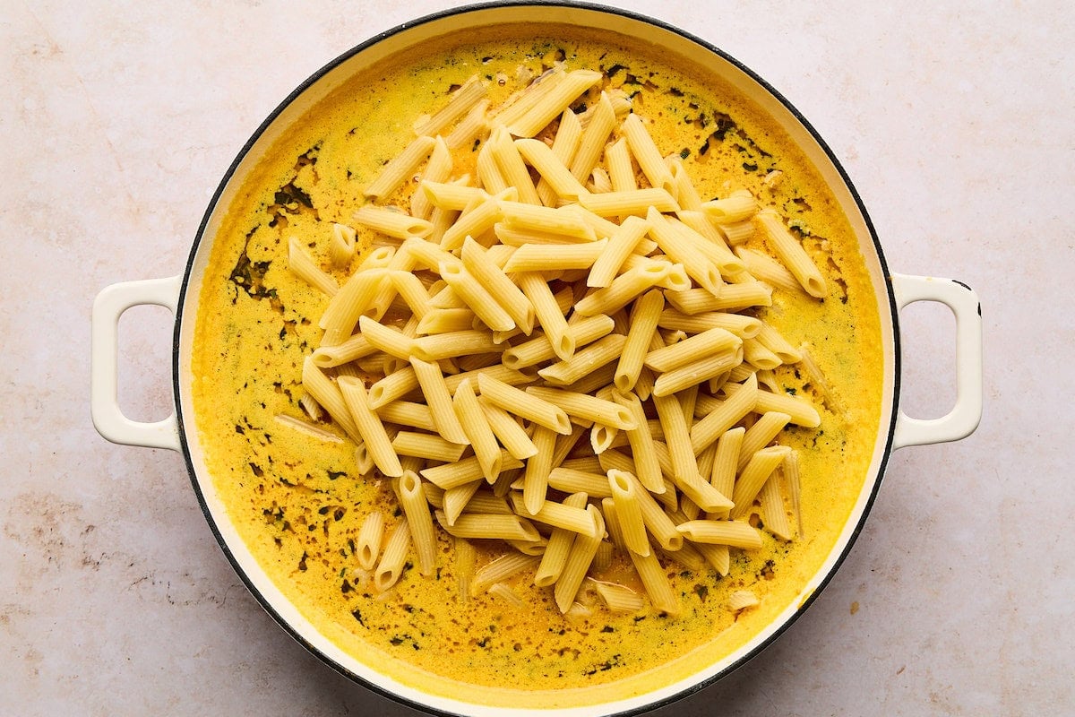 pasta being stirred into pumpkin sauce in large skillet.