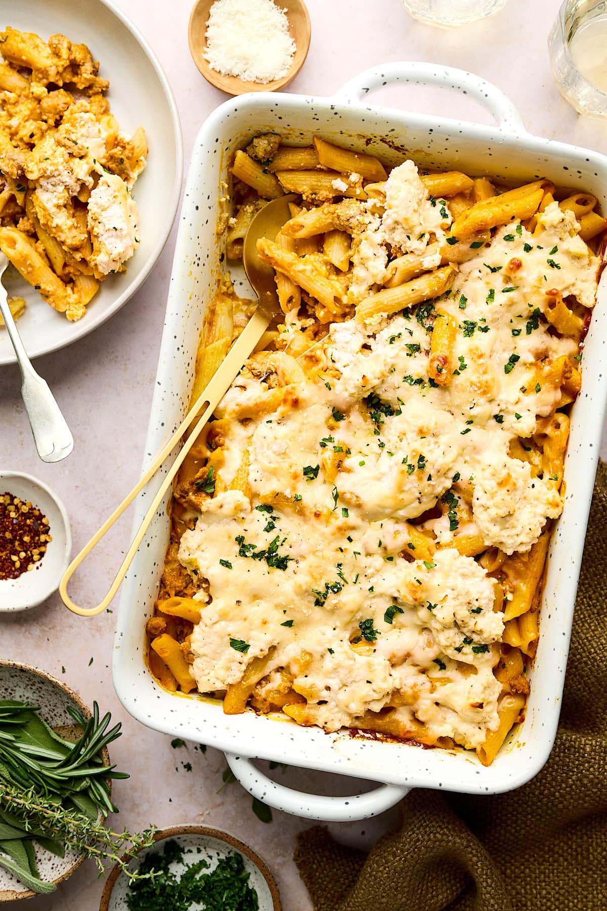 turkey pumpkin pasta bake with cheesy ricotta topping in baking dish with gold serving spoon.